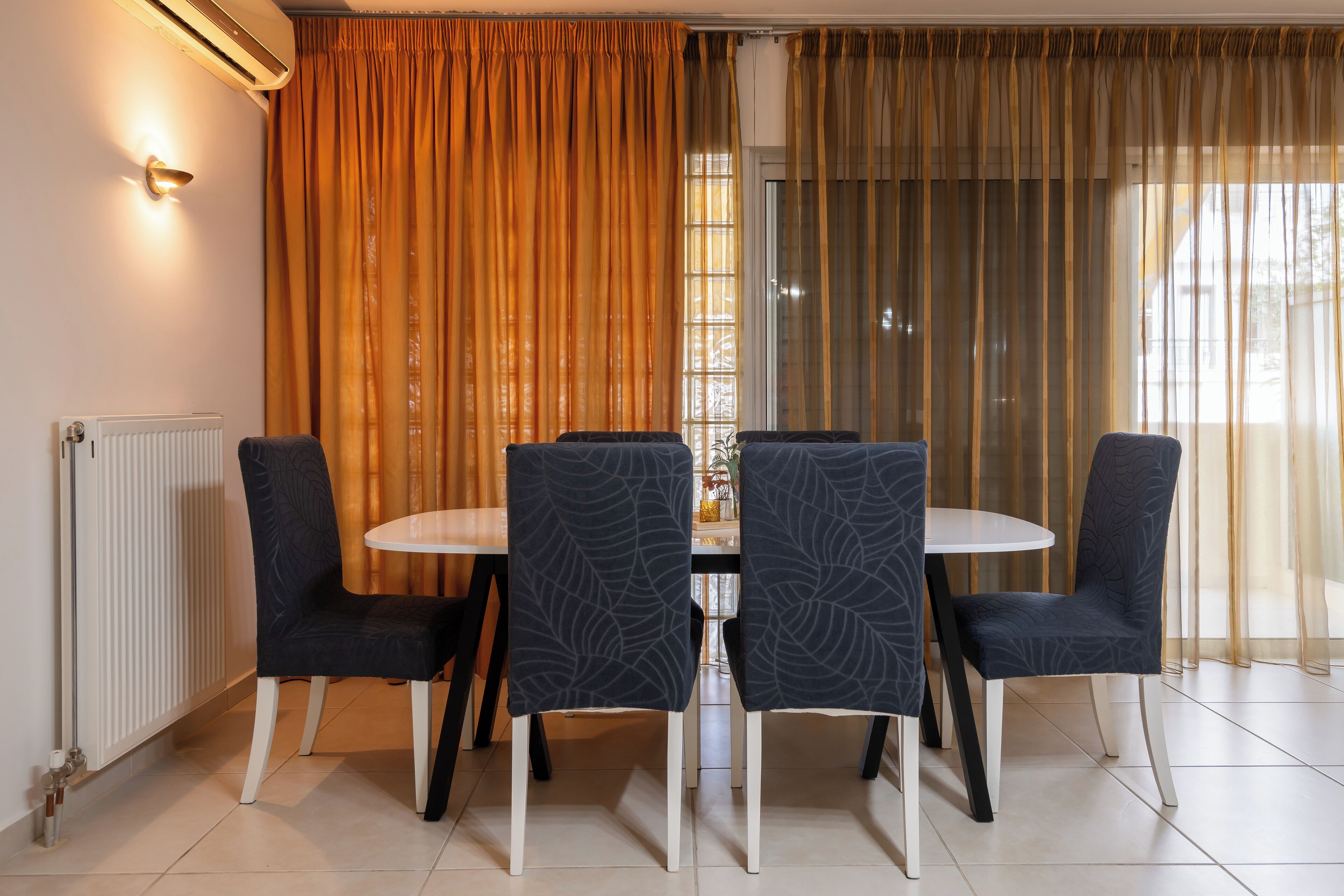 A dining area with a round table and six chairs, a radiator, and a window with curtains.