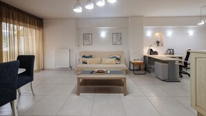 Ein modernes Wohnzimmer mit Sofa, Couchtisch und Essbereich. Es gibt Deckenleuchten, eine Heizung und Kunstwerke an den Wänden.