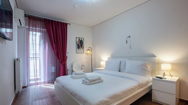 Ein modernes Hotelzimmer mit einem großen Bett, Nachttischen, einem Sessel, einem Fenster mit Vorhängen und einer Wand-Klimaanlage.