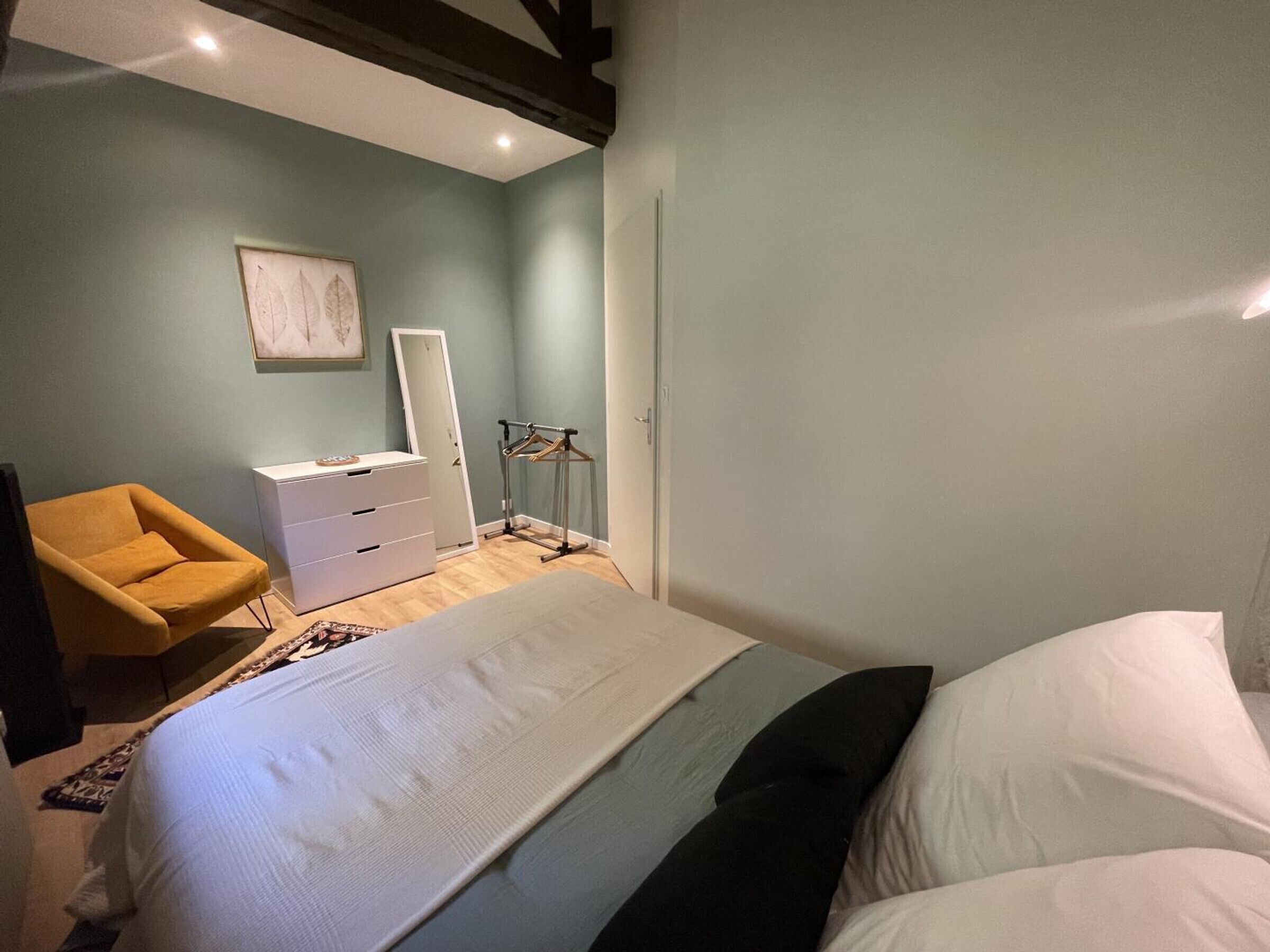 A bedroom with a bed, a dresser, a chair, and a coat rack.