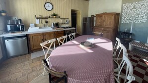 Een keuken met houten kastjes, een eettafel met stoelen, een klok aan de muur en een koelkast.