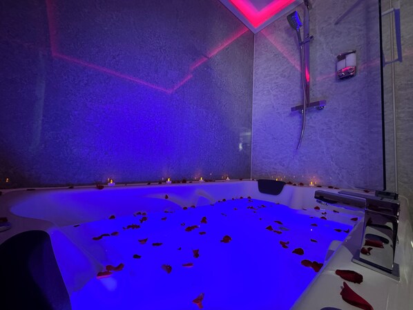 Ein modernes Badezimmer mit einer großen Badewanne, blauer Beleuchtung und Rosenblüten auf dem Boden.