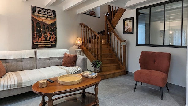 Een woonkamer met een houten trap, een rode fauteuil, een grijze bank en een poster aan de muur.