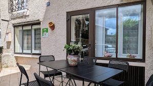 Een buitenterras met een tafel, stoelen, een bloempot en een raam met uitzicht.