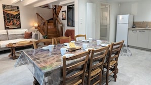 Een eetgedeelte met een tafel voor vier personen, houten stoelen, een tafelkleed met patroon en een trap naar een hoger gelegen niveau.
