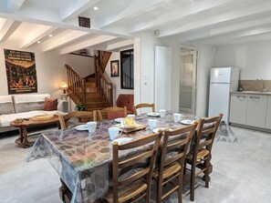 Un coin repas avec une table dressée pour quatre personnes, des chaises en bois, une nappe à motifs et un escalier menant à un niveau supérieur.