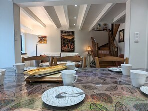 A dining area with a table set for two, featuring a plate with a spoon, a baguette, and several white cups. - Modern family house near Puy-en-Velay with Wifi (Vals-prés-le-Puy)