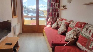 Ein gemütliches Zimmer mit Bett, Fernseher und Blick auf einen verschneiten Berg.