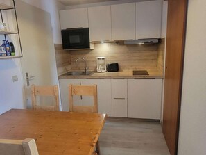 A compact kitchen with white cabinets, a microwave, a coffee maker, and a toaster. There is a wooden table and two chairs. - Cozy apartment for 5 with WIFI in Plagne Soleil (Plagne Soleil)