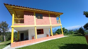 A two-story building with a balcony, a covered porch, and a view of mountains in the background. - Casa linda between mountains and Café: Landscapes, birds and flowers (Andes)