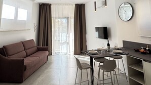 Un saló modern amb un sofà, taula de dinar, cadires i una cuina amb un rellotge i un televisor.