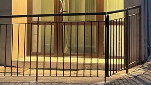 Entrada d'un edifici amb una porta de vidre, una reixa metàl·lica i una petita zona exterior amb paviment de rajoles.