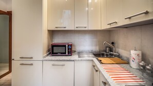 Ett modernt kök med vita skåp, en inbyggd mikrovågsugn, en diskho och en randig skärbräda.