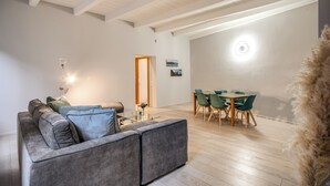 Ett modernt vardagsrum med en grå soffa, ett soffbord i glas och en matplats med ett bord i trä och gröna stolar.