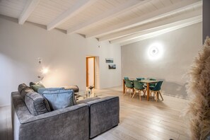 Un salon moderne avec un canapé gris, une table basse en verre et un coin repas comprenant une table en bois et des chaises vertes.