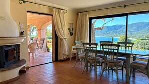 A dining area with a view of a lake and mountains, a fireplace, and a patio with chairs.