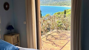 A bedroom with a bed, a nightstand, and a view of a balcony with a scenic landscape.