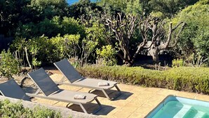 A pool area with lounge chairs and a view of the sea and hills.