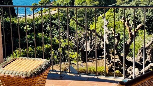 A balcony with wicker furniture overlooking a coastal landscape with mountains and a beach.