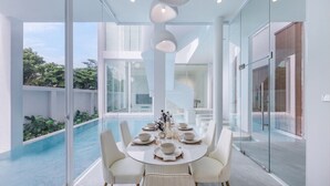 Ein moderner Essbereich mit Glastisch und Stühlen, mit Blick auf einen Swimmingpool und üppiges Grün.