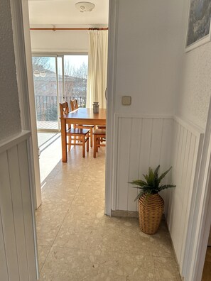 Ein Essbereich mit einem Holztisch und Stühlen, einer Topfpflanze und Blick auf einen Balkon mit Geländer.