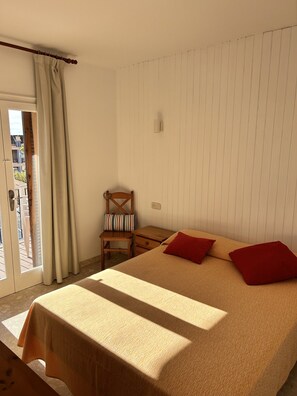 Ein Schlafzimmer mit einem Bett, einem Sessel, einem kleinen Tisch und einem Fenster mit Vorhängen.