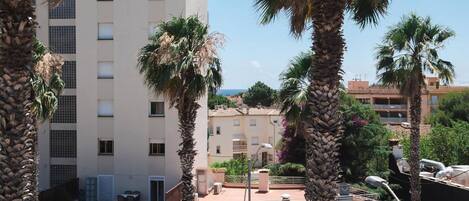 A multi-story building with a flat facade, palm trees in front, and a street with cars and pedestrians.