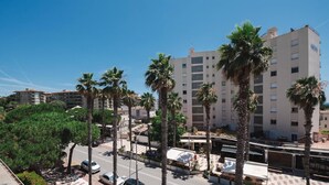 Un hôtel à plusieurs étages au design moderne, agrémenté de palmiers et offrant une vue sur un ciel d’un bleu éclatant.