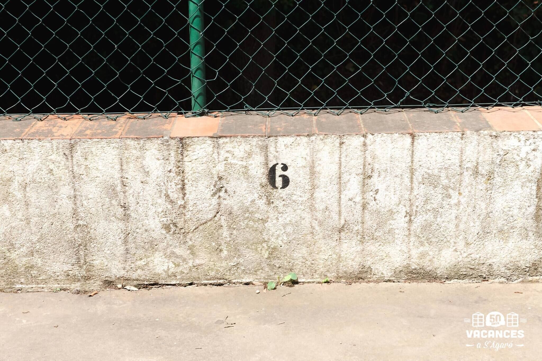 A concrete wall with a metal fence and a green pole.