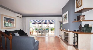 Ein Wohnzimmer mit einer Couch, einem Couchtisch und einem Kamin. Ein Balkon mit gestreiftem Sonnenschirm bietet Blick auf die Stadt.
