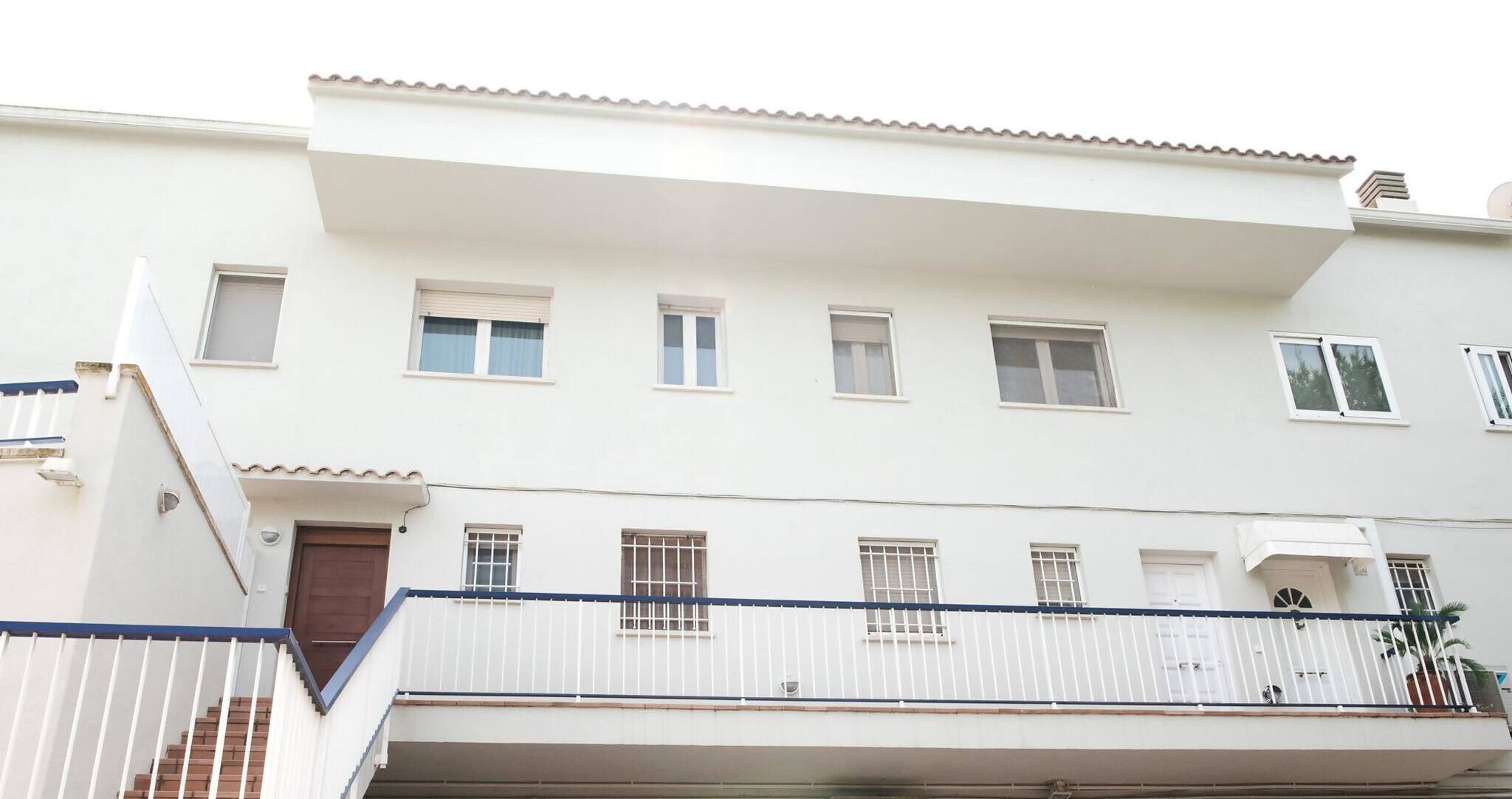 Un edificio residencial de varios pisos con fachada blanca, múltiples ventanas y un balcón con barandilla blanca.