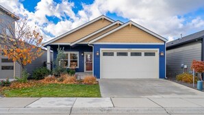 Una casa residenziale con garage, un giardino anteriore con prato e un albero, e un cielo sereno.