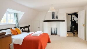Een slaapkamer met een bed, een bureau, een stoel, een open haard en een trap.