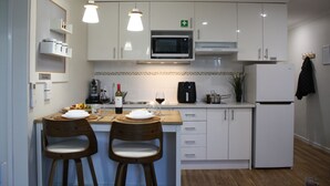 A modern kitchen with white cabinets, a microwave, a coffee maker, and two wooden chairs. - 2BR Apartment with Pool & Tennis Court, Walk to Beach & Shops (Mandurah)