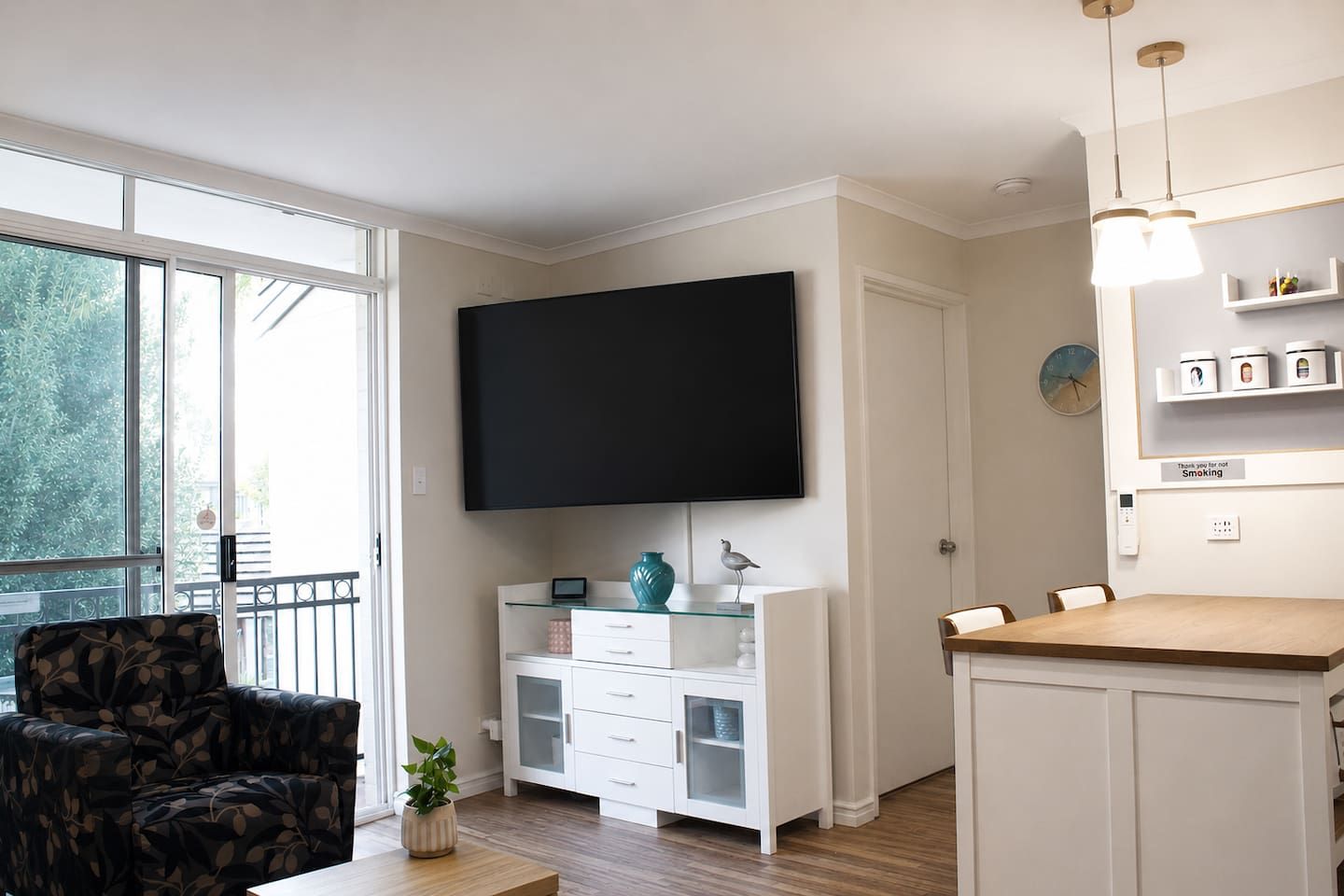Una sala de estar moderna con un televisor de pantalla plana, un sofá, una mesa de comedor y un balcón con barandilla.