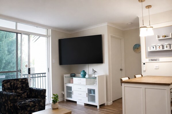 Ein modernes Wohnzimmer mit Fernseher, einer Couch, einem Esstisch und einem Balkon mit Geländer.