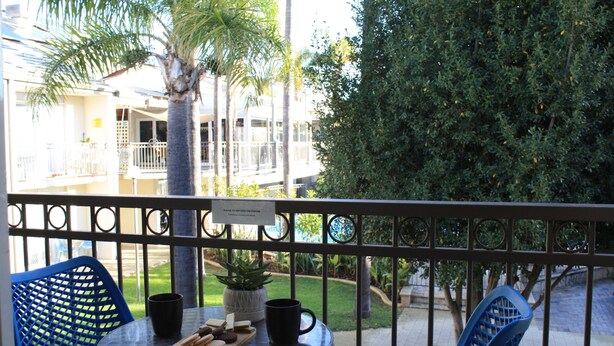 A balcony with a table, chairs, and a potted plant. - 2BR Apartment with Pool & Tennis Court, Walk to Beach & Shops (Mandurah)