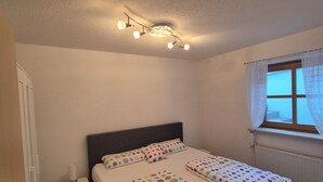Un dormitorio con cama, mesita de noche y ventana con cortinas.