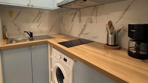 Una cucina compatta con mobili azzurri, una lavatrice integrata, un lavandino e una macchina da caffè.