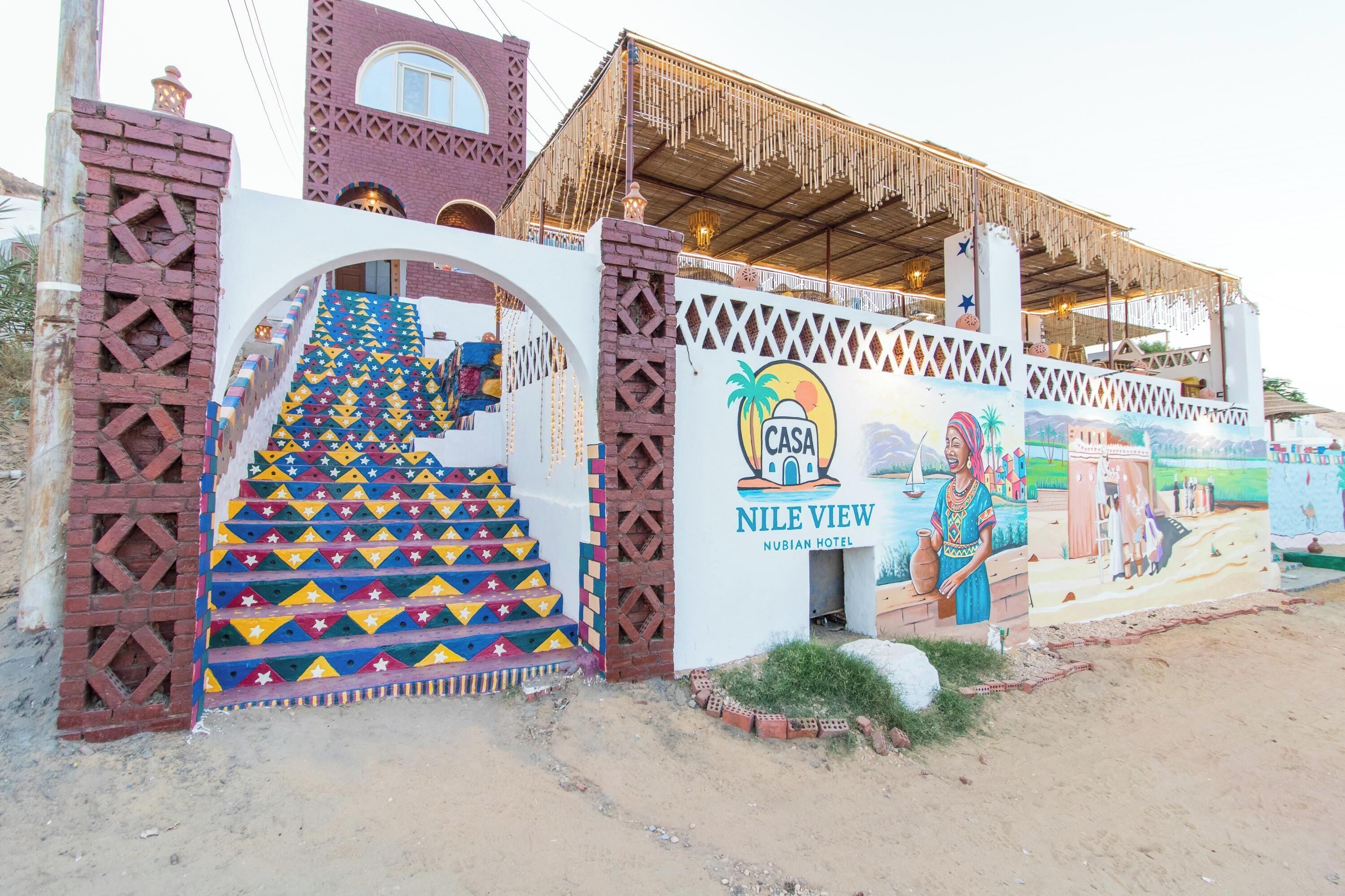 A hotel entrance with a colorful staircase, a mural, and a sign that reads "Nile View Nubian Hotel".