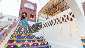 Un escalier aux motifs géométriques colorés mène à un bâtiment dont la façade est en briques rouges et qui présente un mur blanc orné d’un motif en treillis.