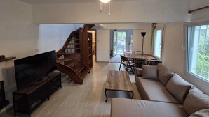 A spacious living room with a TV, sofa, coffee table, and a wooden staircase.