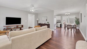 A modern living room with a flat-screen TV, a beige sofa, and a dining area with a table and chairs. - Centerpoint Getaway - The Center of FUN in East TN! (Louisville)