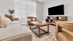 A modern living room with a sofa, a coffee table, and a TV mounted on the wall. - Centerpoint Getaway - The Center of FUN in East TN! (Louisville)