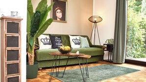 Ein gemütliches Wohnzimmer mit einem grünen Sofa, einem Holzkabinett, einer Stehlampe und einer großen Pflanze.