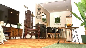 Ein Wohnzimmer mit einem großen Fernseher, einem Holzstuhl, einem Esstisch und einem grünen Teppich.