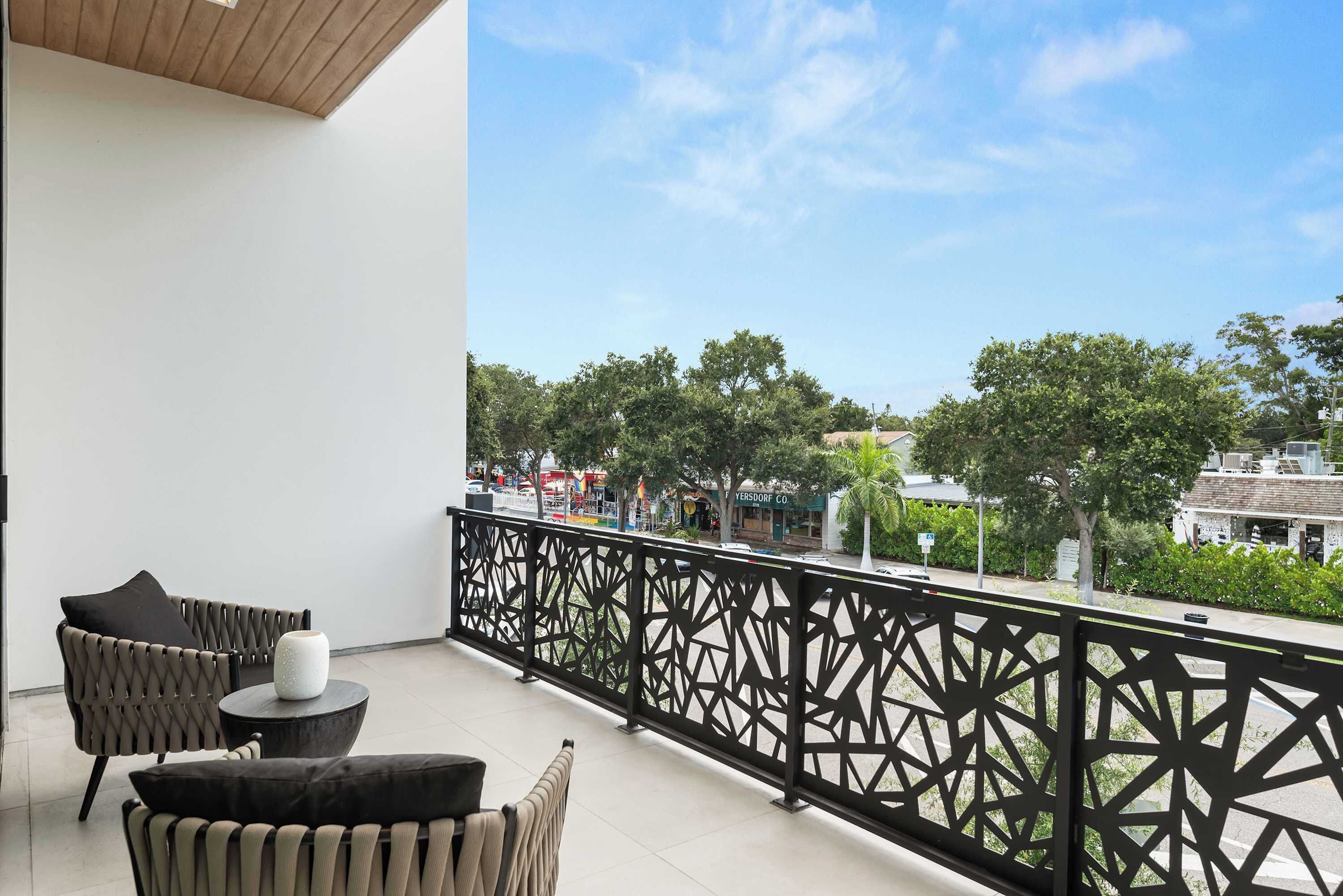 A balcony with a geometric railing, two chairs, and a small table with a vase.