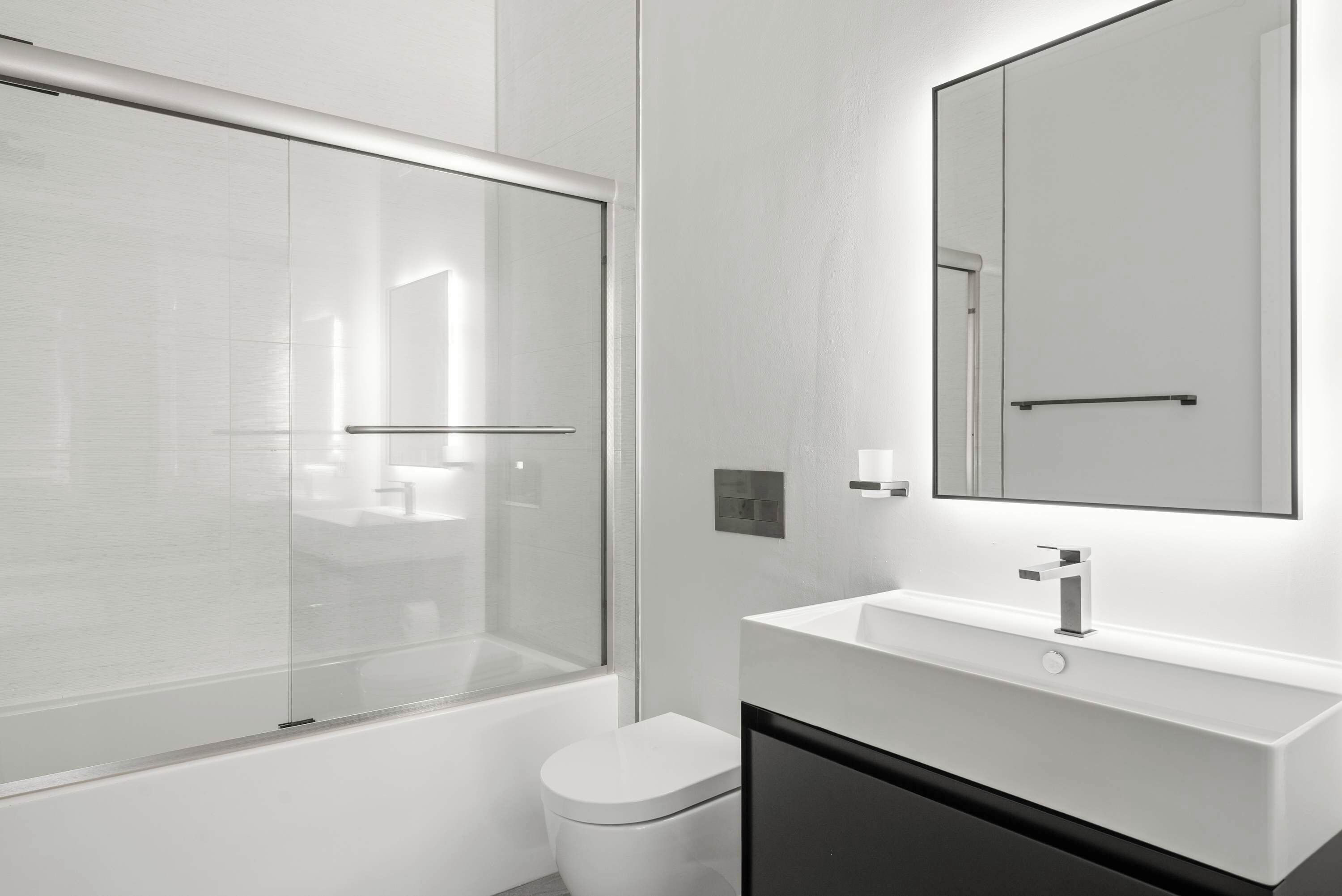Un bany modern amb dutxa envidriada, vàter blanc i un lavabo amb mirall.