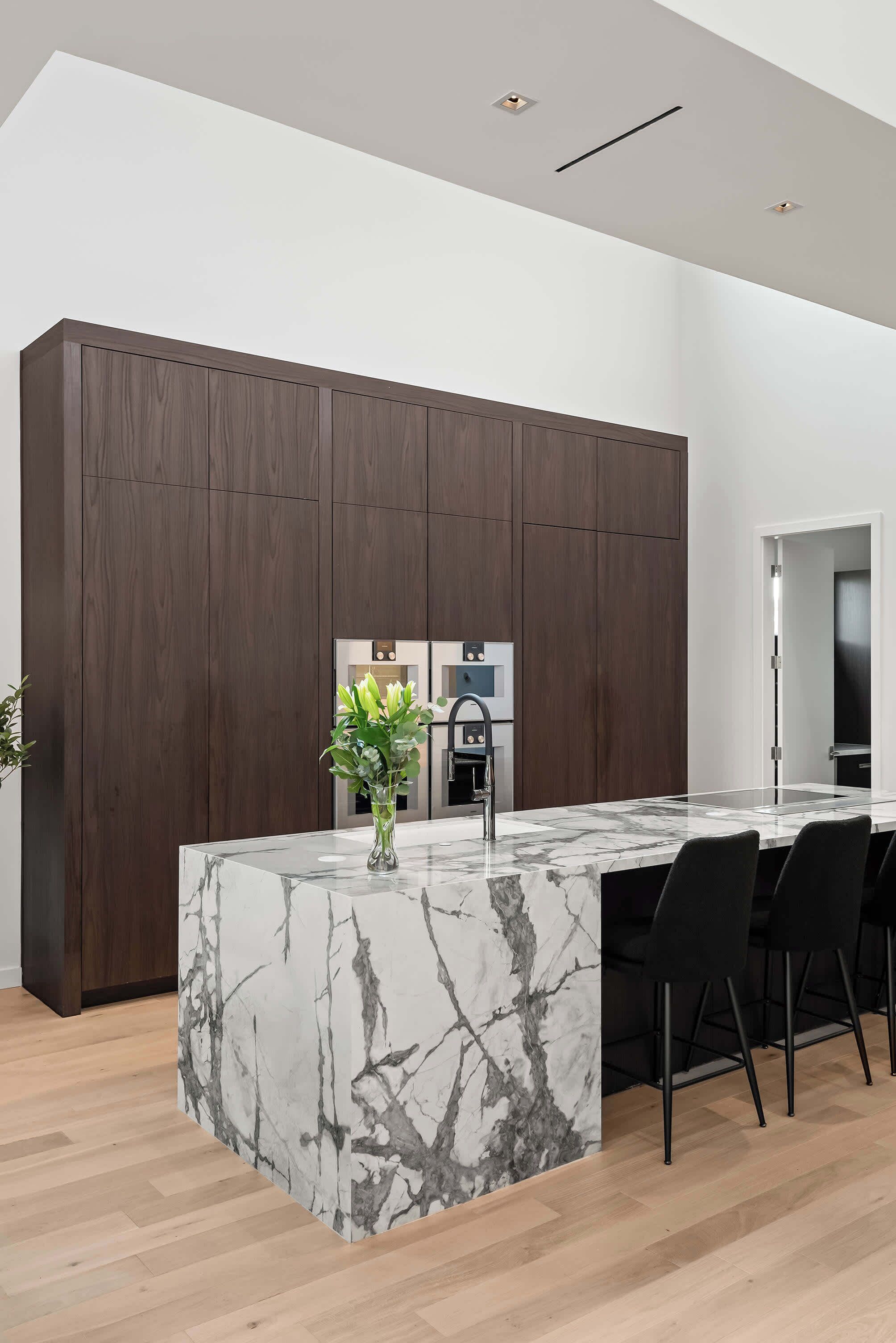 A modern kitchen with a marble island, dark wood cabinetry, and a built-in oven.