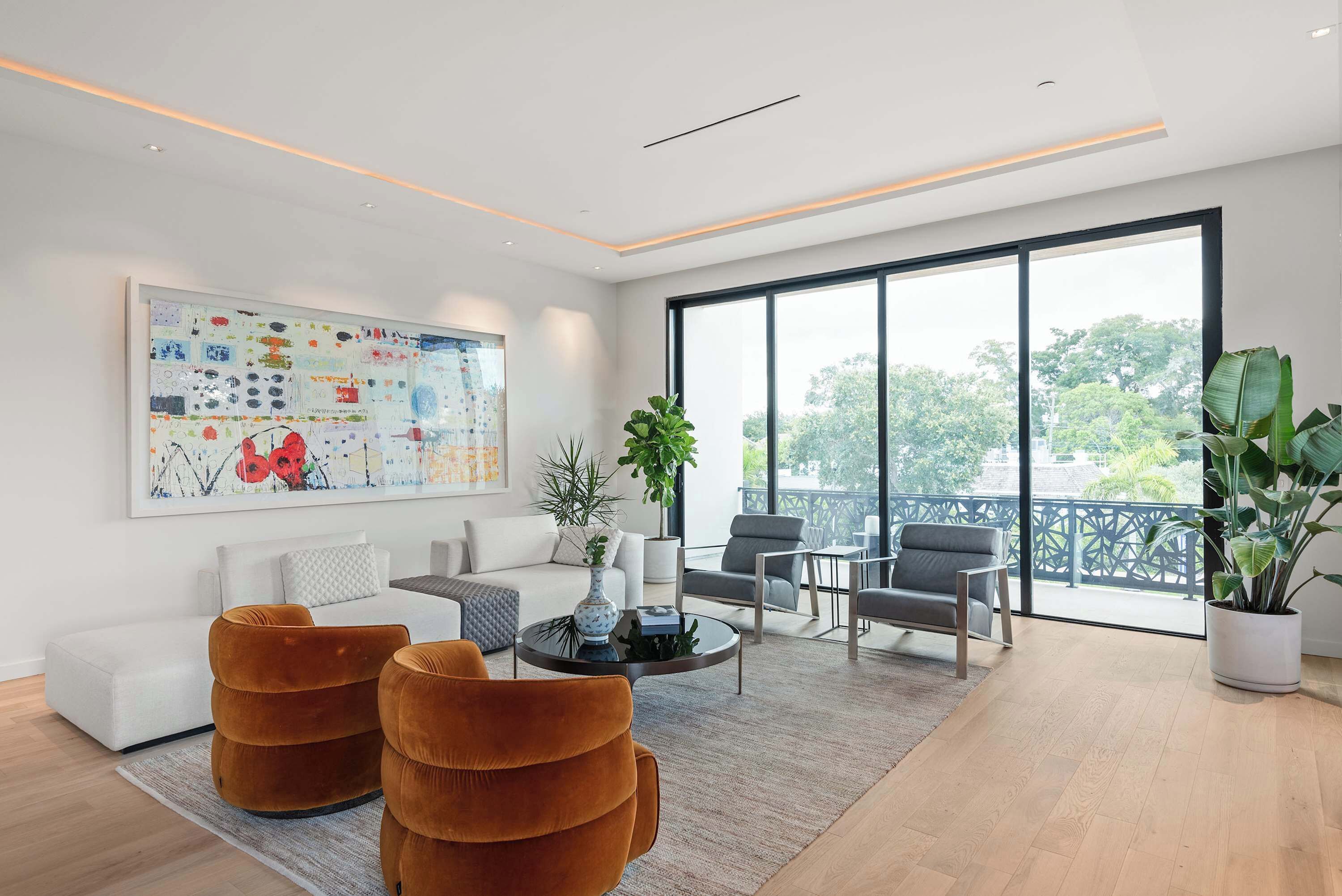 A modern living room with a sofa, two armchairs, a coffee table, and a large window offering a view of trees.